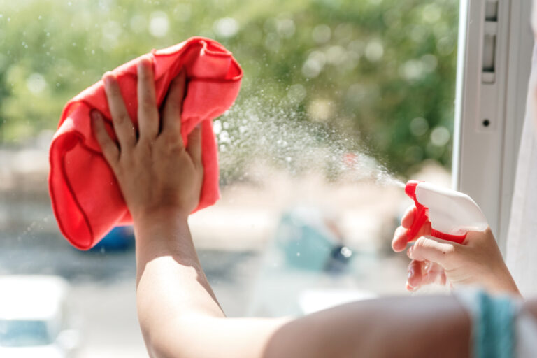 Woman's hand cleaning a window pane with a cloth and window cleaning liquid.